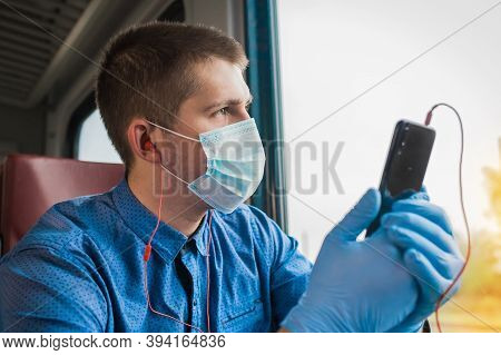 A Guy In A Protective Mask And Medical Gloves Is Holding A Phone And Listening To Music On Headphone