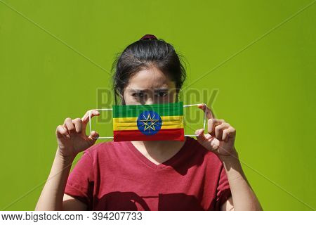 A Woman And Hygienic Mask With Ethiopia Flag Pattern In Her Hand And Raises It To Cover Her Face On 