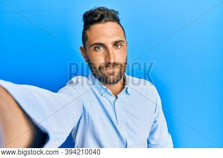 Handsome man with beard taking a selfie photo with smartphone thinking attitude and sober expression looking self confident 
