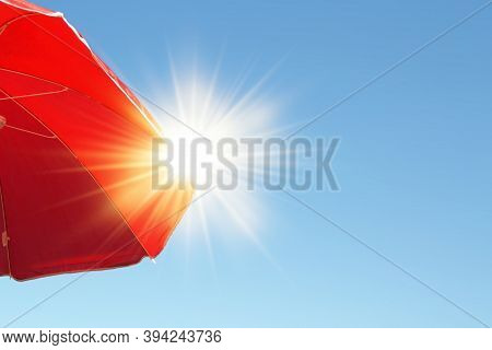 Parasol With Sun Rays.red Beach Umbrella Sheltering The Strong Summer Sun In The Blue Sky.