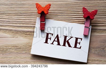Fake - Word On A White Sheet With Beautiful Clothespins On A Wooden Background. Technology Concept