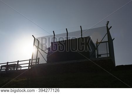Tall Barbed Wire Anti Climb Fence Encases Large Square Metal Industrial Water Management Equipment. 