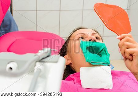 The Patient Holds A Mirror, Sits In A Dental Chair, Examines The Quality Of The Treated Teeth.