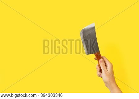 Woman Hand Holding A Small Butcher Axe On A Yellow Background