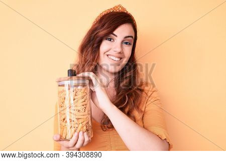 Young beautiful woman holding jar of macaroni pasta looking positive and happy standing and smiling with a confident smile showing teeth 