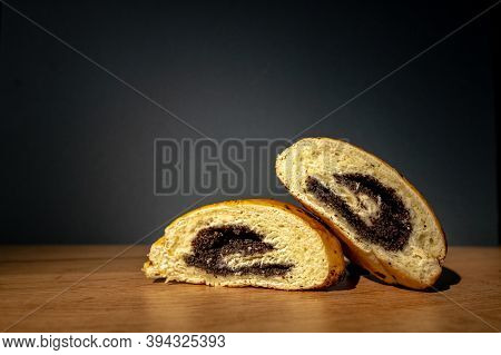 Two Cut Pieces Of A Roll With Poppy Seeds Lie On The Table On A Gray Background