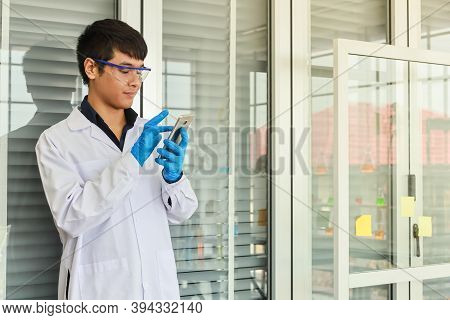 Portrait Of Young Doctor Scientist Wearing Safty Glasses And Blue Rubber Gloves Using Mobile Smartph