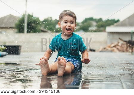 Emotional Caucasian Boy Is Playing With Water On The Ground Smiling At Camera In The Backyard