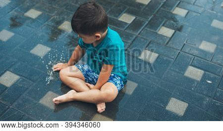 Upper View Photo Of A Caucasian Boy Playing With Water On The Ground After A Rain