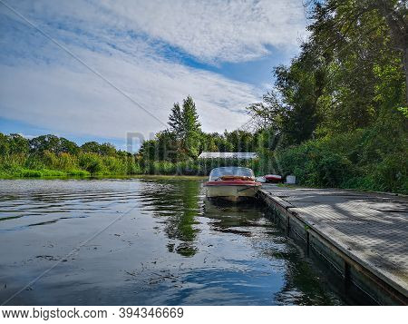 Old Boat Near Wooden Platform On River Between Bushes And Trees