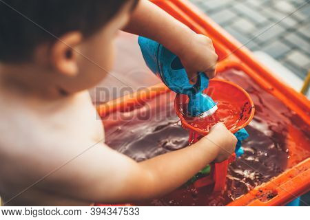 Close Up Photo Of A Caucasian Boy Playing Outside With Water And Plastic Toys Being Undressed In The