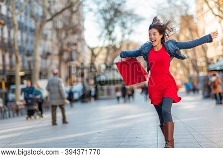 Happy Asian woman walking with shopping bags on Barcelona, La Rambla street. Shopper with open arms up enjoying sale. From tourist destination in Catalonia, Spain travel.