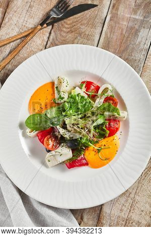Roasted pepper salad with calamari and fresh greens. Rustic wooden table and grey textile