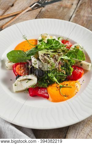 Roasted pepper salad with calamari and fresh greens. Rustic wooden table and grey textile
