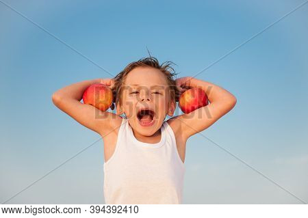 Funny Kid In White Tank Top With Red Apples On Biceps Muscle On Blue Sky Background With Copy Space