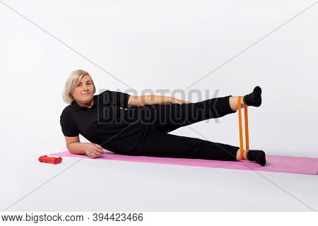 Athletic Senior Woman Doing Fitness Workout At Home With Resistance Rubber Band Lying On Mat. Health