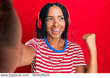 Beautiful hispanic woman taking a selfie photo wearing headphones screaming proud, celebrating victory and success very excited with raised arms 