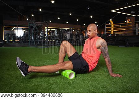 Attractive Young African Male Athlete Relaxing Leg Muscles After Gym Workout, Using Foam Roller. Ath