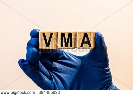 The Word Vma Which Is Made From Wooden Cubes. Hands In A Blue Glove. Isolated On White Background.