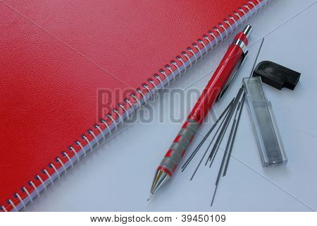 Cuaderno rojo con un lápiz mecánico.