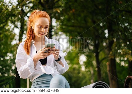 Low-angle Shot Of Smiling Young Woman Browsing Internet On Smartphone. Portrait Of Female Using Mobi