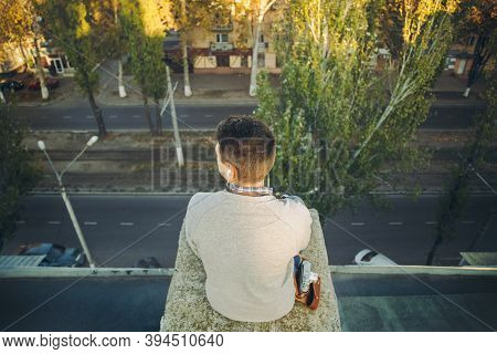 Top View Of A Young Boy, Teenager Sitting Alone On An Edge Of A Building Roof With An Old Photocamer