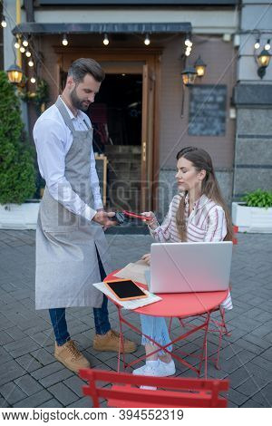 Brown-haired Female Paying Bill Through Payment Terminal In Open Air Cafe