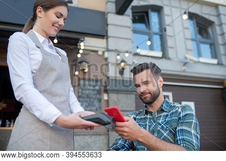 Bearded Male Customer Paying Bill With Smartphone, Waitress Holding Wireless Payment Machine