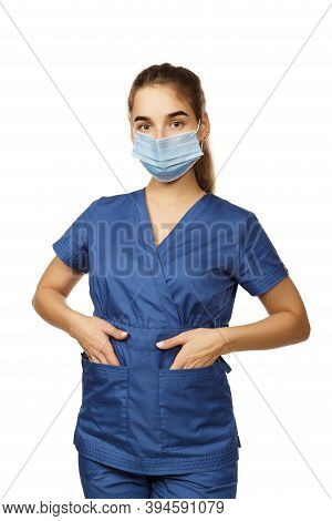 Young Beautiful Female Doctor In A Blue Surgical Gown And A Medical Mask On Her Face Holds Her Hands