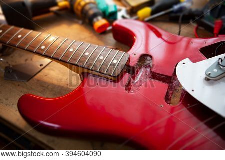 Metallic red electric guitar on guitar repair workbench or a desk,  in repair or maintenance. Pickguard detached. Double cutaway solid body guitar. Shallow depth of field.