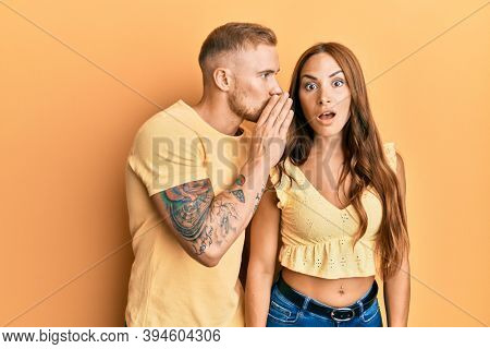 Young couple of girlfriend and boyfriend hugging and standing together hand on mouth telling secret rumor, whispering malicious talk conversation 