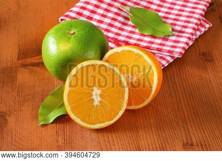 Green grapefruit (sweetie, pomelit, oroblanco), two orange halves and checked red and white tea towel on wooden table