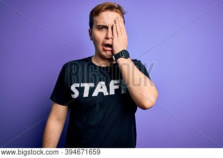 Young handsome redhead worker man wearing staff t-shirt uniform over purple background Yawning tired covering half face, eye and mouth with hand. Face hurts in pain.