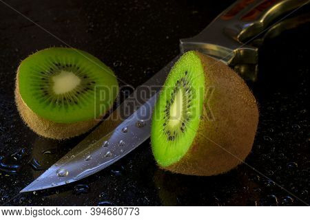 Kiwi Fruit Cut In Half With A Knife And Around The Water Splashes On A Black Background