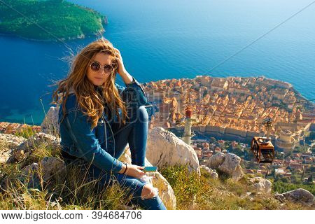 Attractive Brunette Sitting On The Srd Hill Above The City Of Dubrovnik, Observing The City In The D