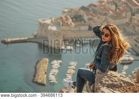 Attractive Brunette Seen From Behind Posing While Sitting On A Stone Above The City Of Dubrovnik, Ou