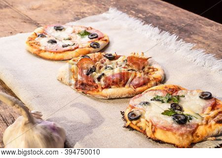 Several Ready-made Mini Pizza, Pizzetta On A Linen Napkin On A Wooden Table