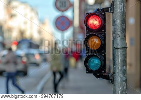 Close-up Of Small Traffic Semaphore With Red Light Against The Backdro Of The City Traffic