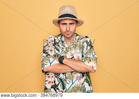 Young handsome man with blue eyes on vacation wearing summer florar shirt and hat skeptic and nervous, disapproving expression on face with crossed arms. Negative person.