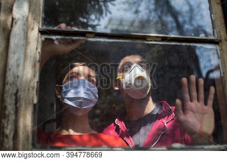 Family Quaranteaming,young Caucasian Couple Wearing Protective Medical Masks Looking Through The Win