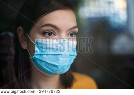 Anxious Depressed And Stressed Young Woman Wearing Medical Face Mask,in Home Isolation Looking Outsi