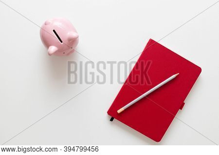 Creative Flat Lay Photo Of Red Notebook, Pen And Piggy Bank On A White Minimalistic Background With 