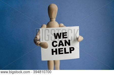 The Wooden Man Holds A White Sign With The Text We Can Help In His Hands. The Content Of The Letteri