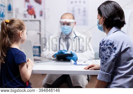 Pediatrician Wearing Face Mask Holding Tablet Pc While Consulting Child During Clobal Pandemic With 