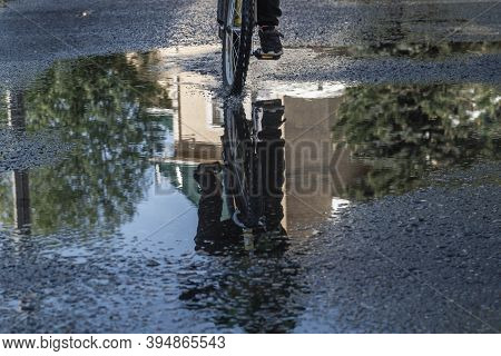 A Man Rides A Bicycle On The Road. Puddles On The Asphalt After The Rain. Splashes And Drops Of Wate
