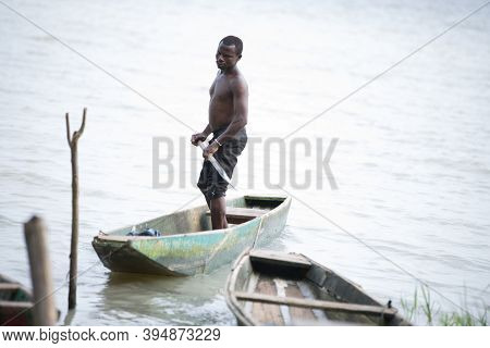 Abidjan, Ivory Coast -11 February 2018: Shirtless Young Man Standing In A Dugout Canoe On The Water 