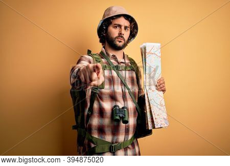 Young hiker man with curly hair and beard hiking wearing water canteen using city map pointing with finger to the camera and to you, hand sign, positive and confident gesture from the front