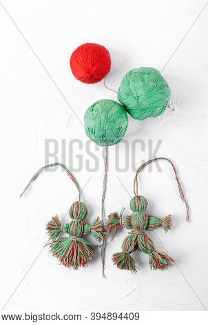 Handmade Dolls Of Red And Green Threads On The White Table. Martenichki, Slavic Mascots Symbolising 