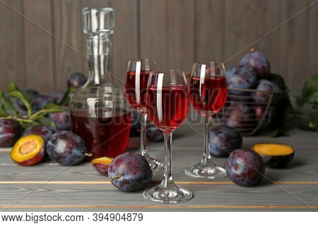 Delicious Plum Liquor And Ripe Fruits On Grey Wooden Table. Homemade Strong Alcoholic Beverage