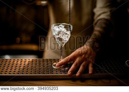 Close-up Of Glass With Ice Cubes Being Stirred By Bartender With Long Bar Spoon